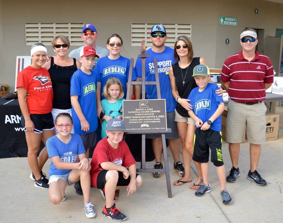 Gator Redleg families and players in REDLEG jerseys gathered around the Kenny A. Fike memorial plaque at the softball tournament.
